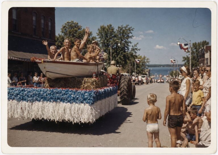 Children waving from a rowboat float in the Lake Days parade, the lake at the end of the street, circa 1965