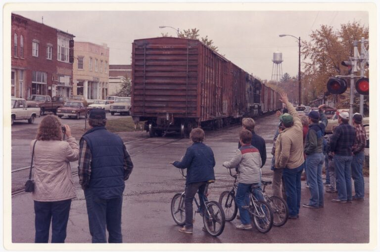 Townspeople waving from the crossing as the last freight train leaves town, 1983