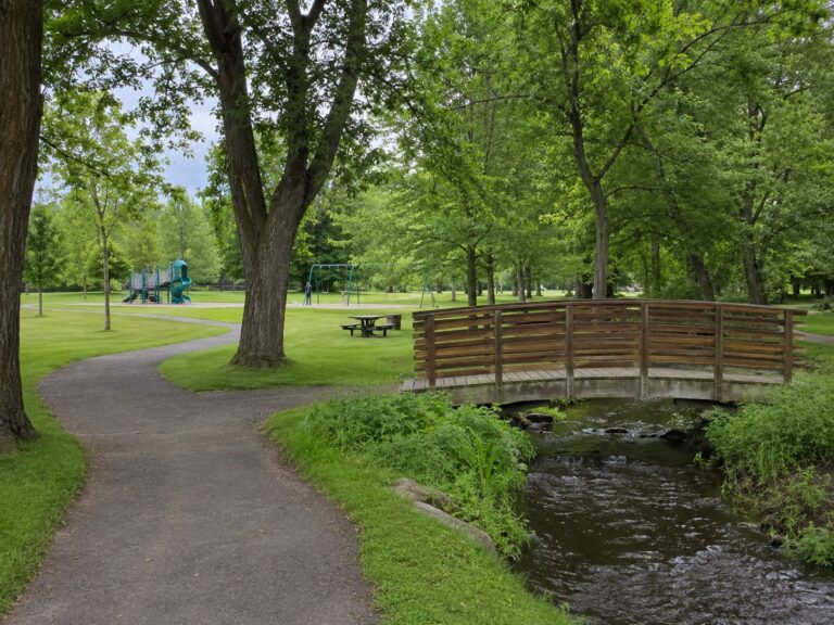 Riverside Park: the wooden footbridge over the creek, the walking trail, playground and swings in the distance